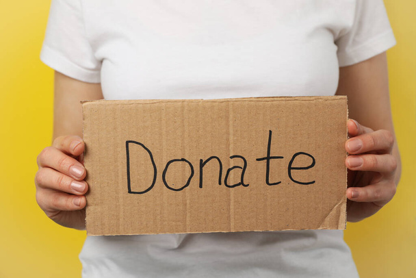 Woman holds cardboard with text Donate on yellow background - Photo, image
