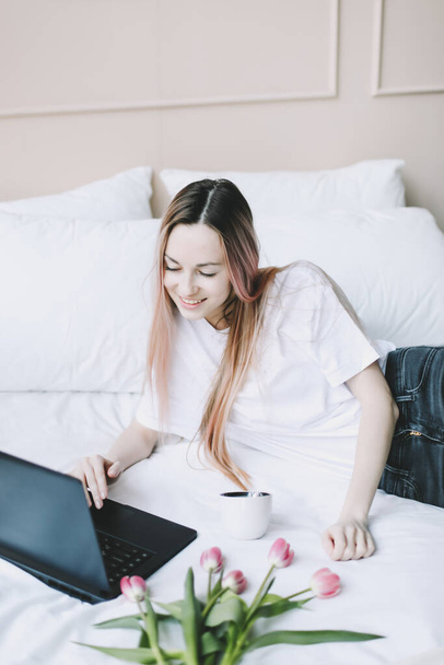 Young woman working on laptop in bed with white linens. Lifestyle composition. Working at home, quarantine concept.  - Foto, Imagem