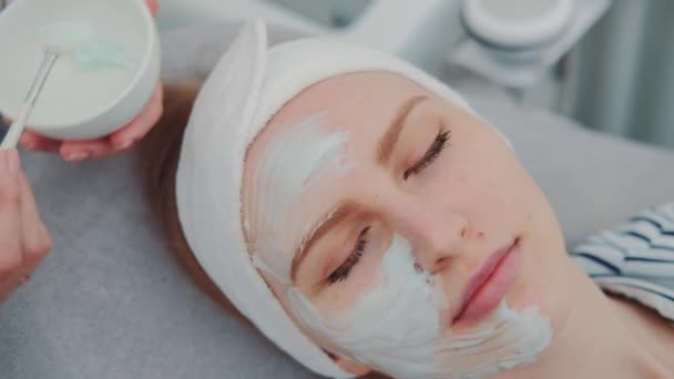 Primer plano de las manos Cosmetician aplicación de máscara de crema en la cara de las mujeres jóvenes en el salón de spa de belleza
 - Metraje, vídeo