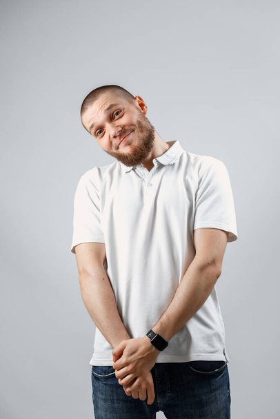 Retrato de un joven tímido guapo con una camiseta blanca sobre un fondo gris. aislado. Espacio de copia
 - Foto, imagen