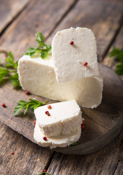Suluguni cheese is cut into large pieces on a wooden round board. Garnished with parsley leaves,  and pepper. - Foto, immagini