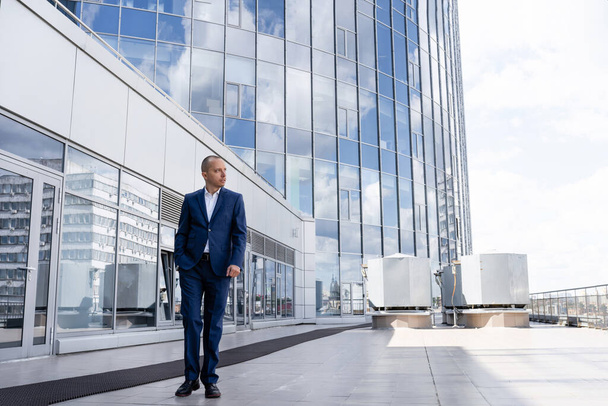 Business man in the city near the business center. A young man in a business suit near a large blue office center. Business man near a large modern glass building - Foto, Imagen
