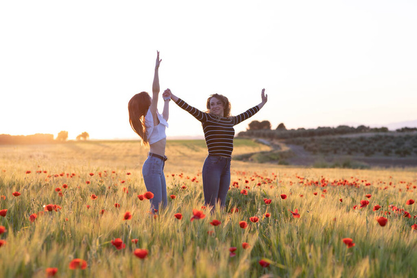ケシ畑で日没時にジャンプする2人の女の子 - 写真・画像