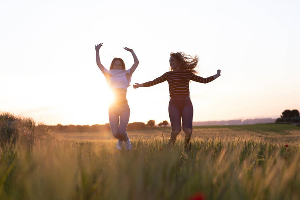 deux filles sautant au coucher du soleil dans le champ
 - Photo, image