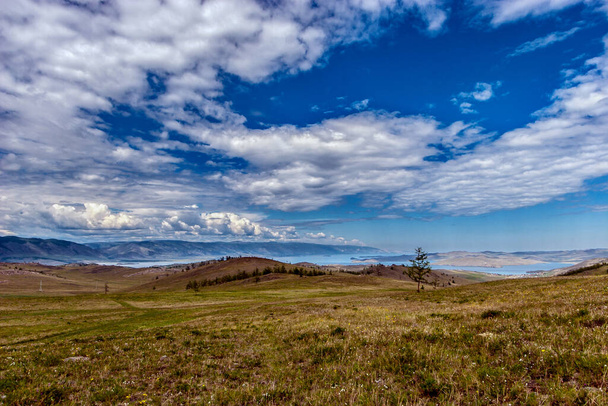 Удивительный пейзаж холмов возле озера Байкал и облака против голубого неба. Зеленая трава на земле. Вдали от гор. Горизонталь
. - Фото, изображение