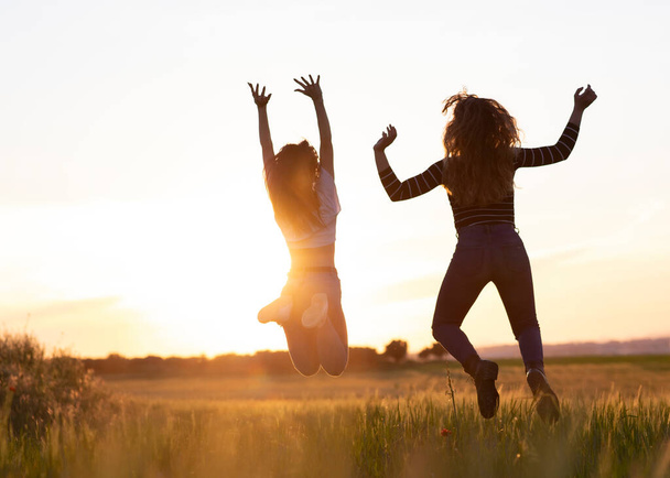 Két lány ugrál napnyugtakor a mezőn. - Fotó, kép