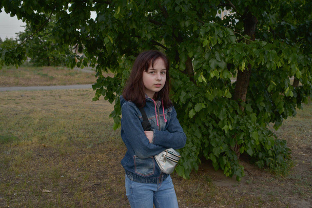 Outdoor grappige portret van een schattig klein 9-10 jaar oud meisje dragen denim. Meisje van negen op straat. Portret van een meisje van 9 of 10 jaar tegen de achtergrond van bomen in het voorjaar. Schoolmeisje. - Foto, afbeelding