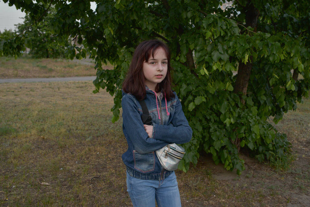 Kot giyen 9-10 yaşlarında sevimli bir kızın açık havada çekilmiş komik portresi. Sokakta 9 yaşında bir kız. 9 ya da 10 yaşındaki bir kızın portresi baharda ağaçların arka planında. Öğrenci kız. - Fotoğraf, Görsel