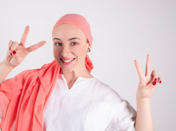 schöne Frau, Kämpferin gegen den Krebs, trägt einen rosafarbenen Schal, macht mit den Fingern ein Siegessymbol - Foto, Bild