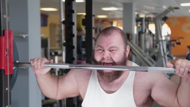 Een grote en krachtige gewichtheffer bijt de lange halter boos voor het doen van de oefening. - Video