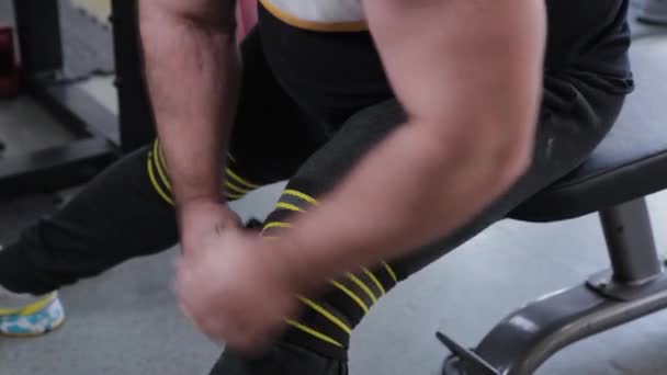 Big and powerful weightlifter wraps elastic hard bandages on his knees. - Felvétel, videó