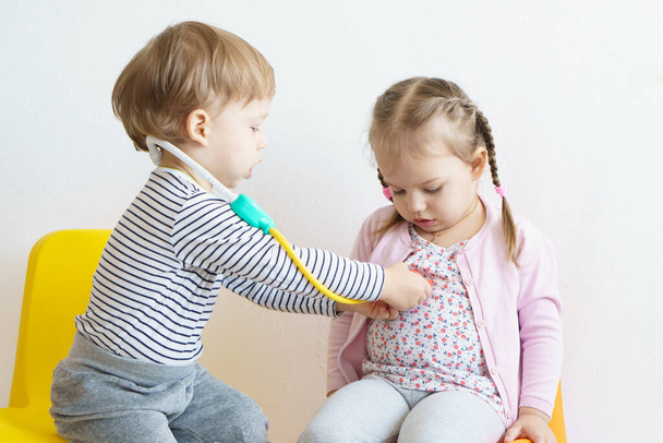 Két gyerek orvososdit játszik a gyerekszobában. A sárga szemüveges testvér kezeli a húgát, fogorvost játszik, fül-orr-gégészt, szemészt, lázmérőt. Szerepjáték játékok gyerekeknek, a fejlesztés - Fotó, kép