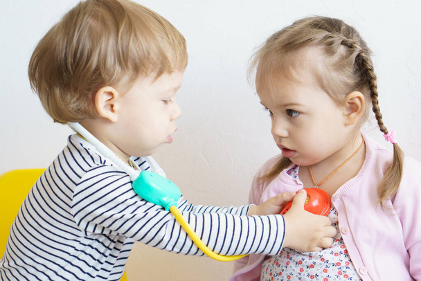Two children play doctor in the nursery. Brother in yellow glasses treats his sister, playing dentist, ENT, ophthalmologist, temperature measurement. Role-playing games for children, the development - Foto, Imagem