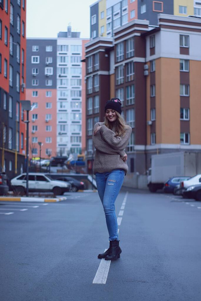 Городской портрет счастливой флиртующей красивой женщины в вязаном коричневом свитере, джинсах и черной шляпе. на парковке
 - Фото, изображение