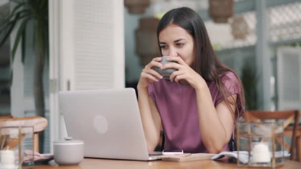 Portrait of young woman sitting with laptop and drinks coffee in cafe - Video