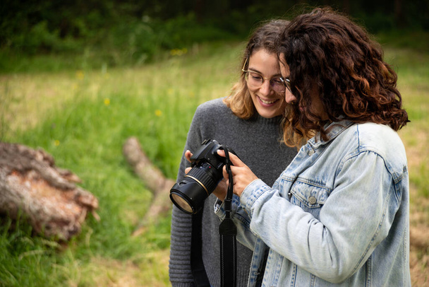Dos mujeres blancas jóvenes en el parque mirando alegremente las fotos tomadas en su cámara digital
. - Foto, Imagen