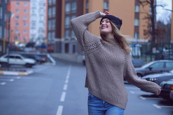 retrato urbano de uma mulher bonita sedutora feliz em suéter marrom de malha, jeans e chapéu preto. no estacionamento
 - Foto, Imagem