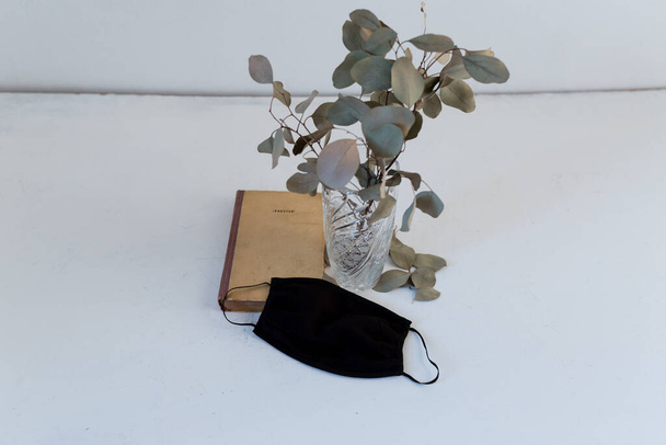 száraz eukaliptusz egy vázában egy könyv, fekete maszk - Fotó, kép