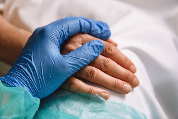Nahaufnahme einer Arzthand mit blauem Handschuh, die einem Patienten im Krankenhaus Halt und Liebe gibt. Coronavirus-Pandemiekonzept.  - Foto, Bild
