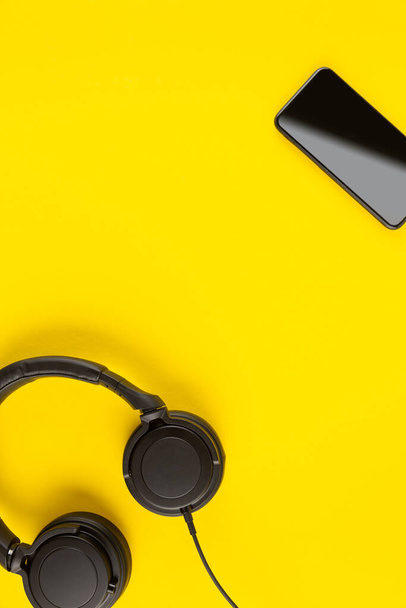 Μαύρο smartphone και ακουστικά σε αφηρημένο κίτρινο πολύχρωμο φόντο με χώρο για κείμενο. Εφαρμογή δημιουργικής μουσικής ελάχιστη έννοια. - Φωτογραφία, εικόνα