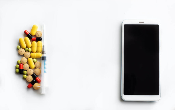 Multi-barevné tablety a tobolky různých tvarů s injekční stříkačkou na levém okraji a mobilním telefonem na pravém okraji s místem pro zobrazení na horním okraji textu. - Fotografie, Obrázek