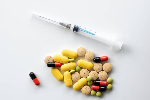 Verschillende gekleurde pillen en capsules van verschillende vormen en een spuit bovenaanzicht - Foto, afbeelding