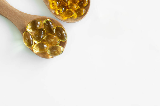 At the top of the edge there are 2 wooden spoons with capsules of fish oil Omega-3 and vitamin D3 large and small. Top view and free space for text. Isolated - Photo, Image