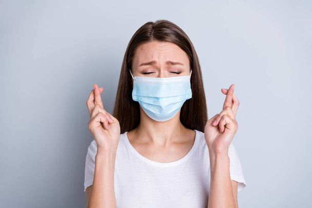 Photo of pretty lady had contact infected people hospital examination patient terrified eyes closed fingers crossed praying good results wear protect face mask isolated grey color background - Foto, immagini