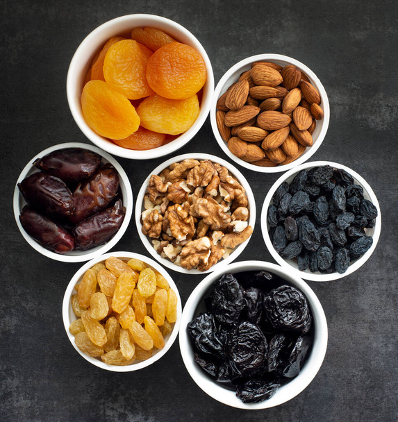 Frutas secas en cuencos blancos sobre un fondo oscuro para mantener la salud cardiovascular vista superior
 - Foto, Imagen
