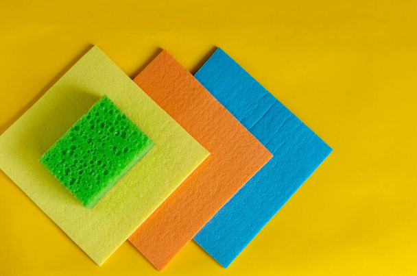 Kitchen porous sponges and napkins. Multi-colored kitchen napkins for cleaning and sponges on yellow. A set of new bright accessories for cleaning. Commercial cleaning company. Selective focus. - 写真・画像