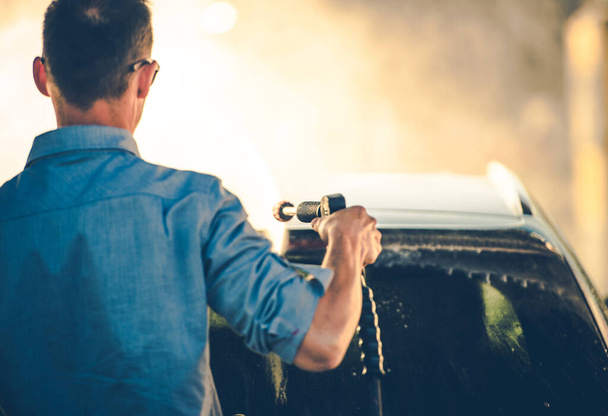 Автомобильная тема. Весеннее время мойки автомобилей с помощью мойки под давлением. Кавказские мужчины чистят его современный компактный автомобиль. - Фото, изображение