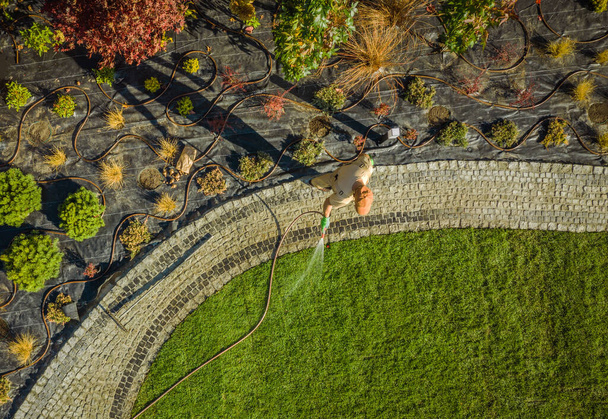 Кавказский садоводческий работник поливает недавно установленную естественную траву. Ландшафтный дизайн. Аэрофотосъемка
. - Фото, изображение
