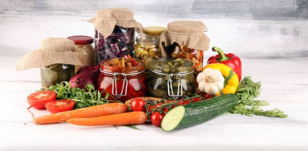 Conserva verduras en frascos de vidrio. Pepino en escabeche, zanahoria, col fermentada y cebollas sobre mesa rústica
 - Foto, imagen