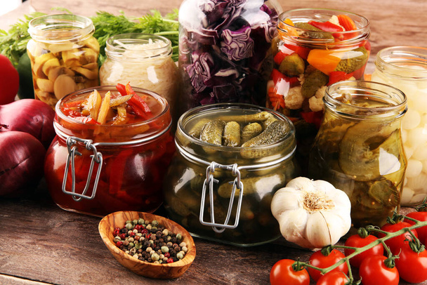 Preserva legumes em frascos de vidro. Pepino em conserva, cenoura, repolho fermentado e cebola na mesa rústica
 - Foto, Imagem