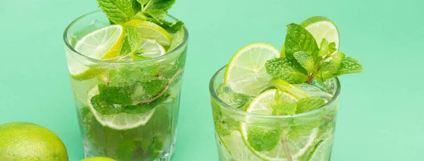 Refrescantes bebidas de cóctel Mojito en los vasos con limas frescas en rodajas y hojas de menta sobre fondo de pancarta verde
 - Foto, imagen