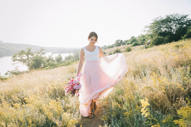 Novia en un lujoso vestido de novia blanco y rosa en la naturaleza al atardecer
 - Foto, Imagen