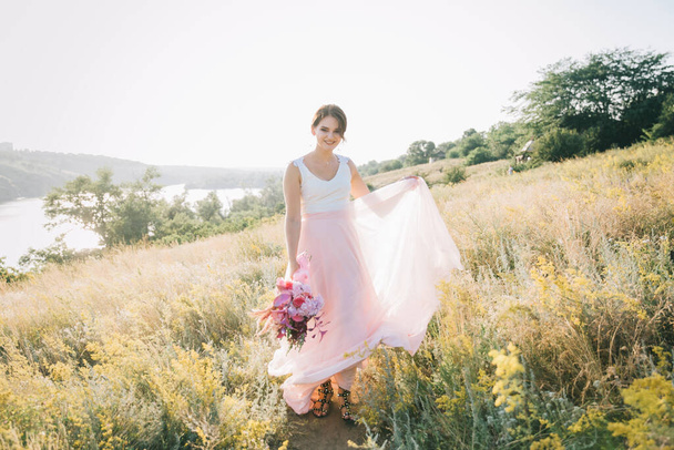 Noiva em um luxuoso vestido de noiva branco e rosa na natureza ao pôr do sol
 - Foto, Imagem