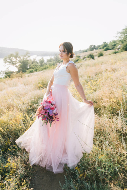 Novia en un lujoso vestido de novia blanco y rosa en la naturaleza al atardecer
 - Foto, imagen
