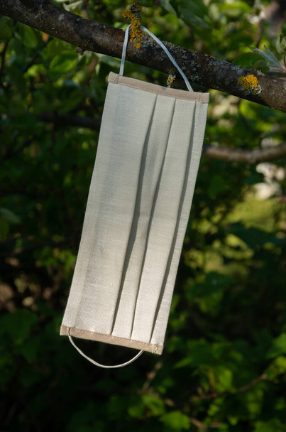 Wit gezichtsmasker dat aan een boom hangt, covid-19 coronavirus - Foto, afbeelding