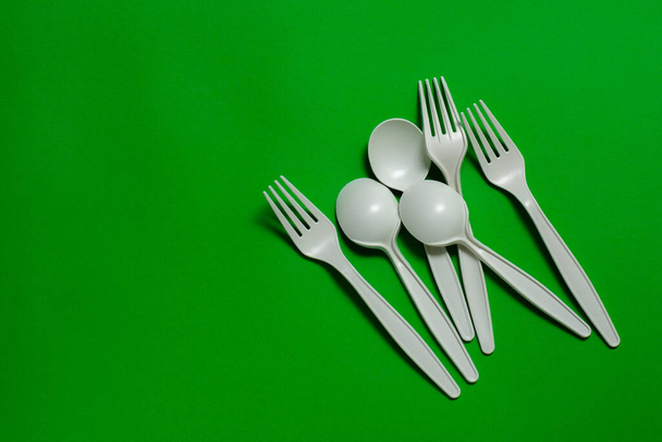 eco-friendly disposable tableware on a green background. isolate. three spoons and forks of corn starch. biodegradable dishes. natural materials for replacing plastic. place for text - Photo, Image
