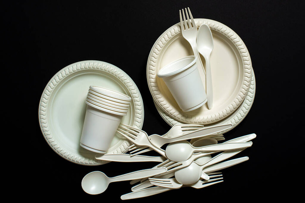 Sets of biodegradable disposable tableware on a black background. Spoons, forks, plates, glasses of corn starch. isolate. environmentally friendly modern ecological biomaterials, plastic replacement. place for text - Photo, Image