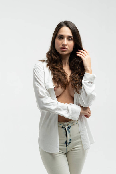 young beautiful girl pose in a white shirt and white jeans in the studio - Фото, изображение