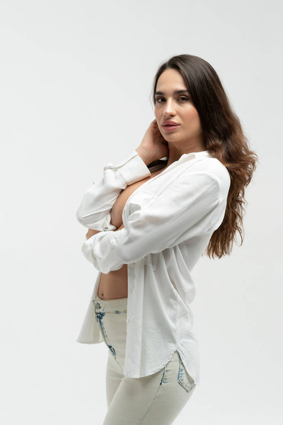 young beautiful girl pose in a white shirt and white jeans in the studio - Φωτογραφία, εικόνα