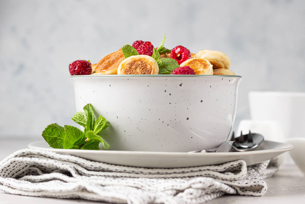Bowl with tiny pancake cereal with raspberries, mint and jam on a grey concrete background. Trendy food. Mini cereal pancakes. Pancake porridge. - Photo, Image