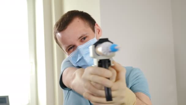 Egy férfi maszkos fogorvos portréja, aki mosolygó szájfecskendővel a kamerát nézi. Fogászati szakember fogászati eszközökkel a munkahelyen. Fogászati fogászati kezelésben részesülő orvos - Felvétel, videó