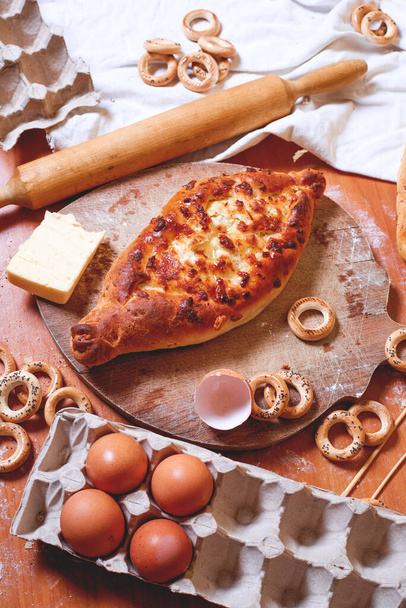Top view of a delicious traditional Ajarian khachapuri-an open baked pie with melted salted Suluguni cheese and egg yolk on a wooden tray on the table during cooking. Traditional Georgian cuisine - Foto, Imagem