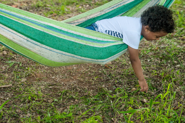 африканський молодий хлопчик грає на гамаку, торкаючись трави своїми руками
. - Фото, зображення