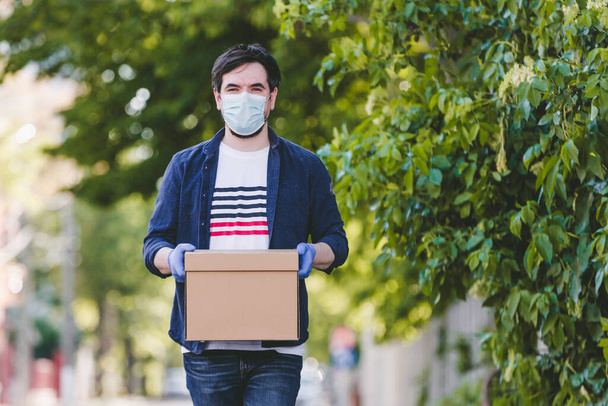 Repartidor sosteniendo una caja de comida sobre un fondo verde, repartidor de comida hombre con máscara protectora y guantes
 - Foto, imagen