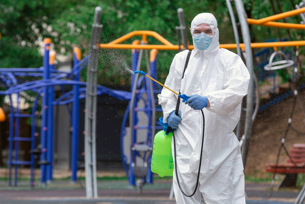 Mann in Schutzanzug desinfiziert Spielplatz mit Sprühchemikalien, um Ausbreitung des Coronavirus zu verhindern, Pandemie in Quarantäne-Stadt. - Foto, Bild