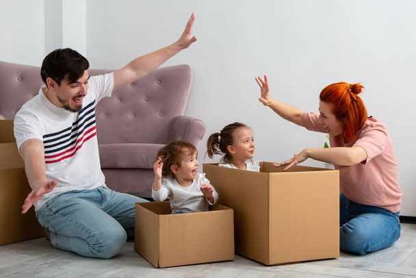 Hauska aktiivinen perhe leikkii muuttopäivänä, innoissaan onnellinen aikuinen vanhemmat äiti isä leikkii pahvilaatikoita söpö pienet lapset istua sisällä hauskaa pakkaus siirtää uuteen kotiin concep - Valokuva, kuva